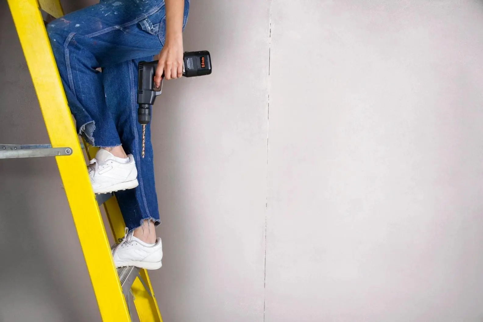 A person is sitting on the ladder holding a drill.